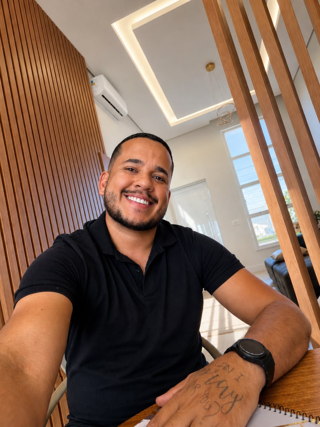 Lucas Zaros sorrindo, sentado em uma casa com painel de madeira